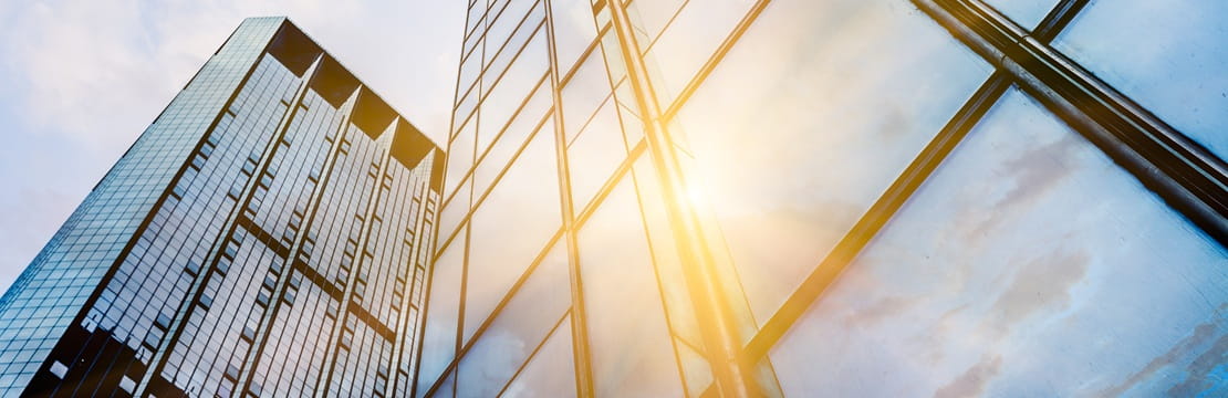 Upward view of modern glass skyscrapers reflecting sunlight and blue sky.