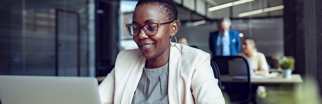 Woman sits at a desk in front of a laptop. 